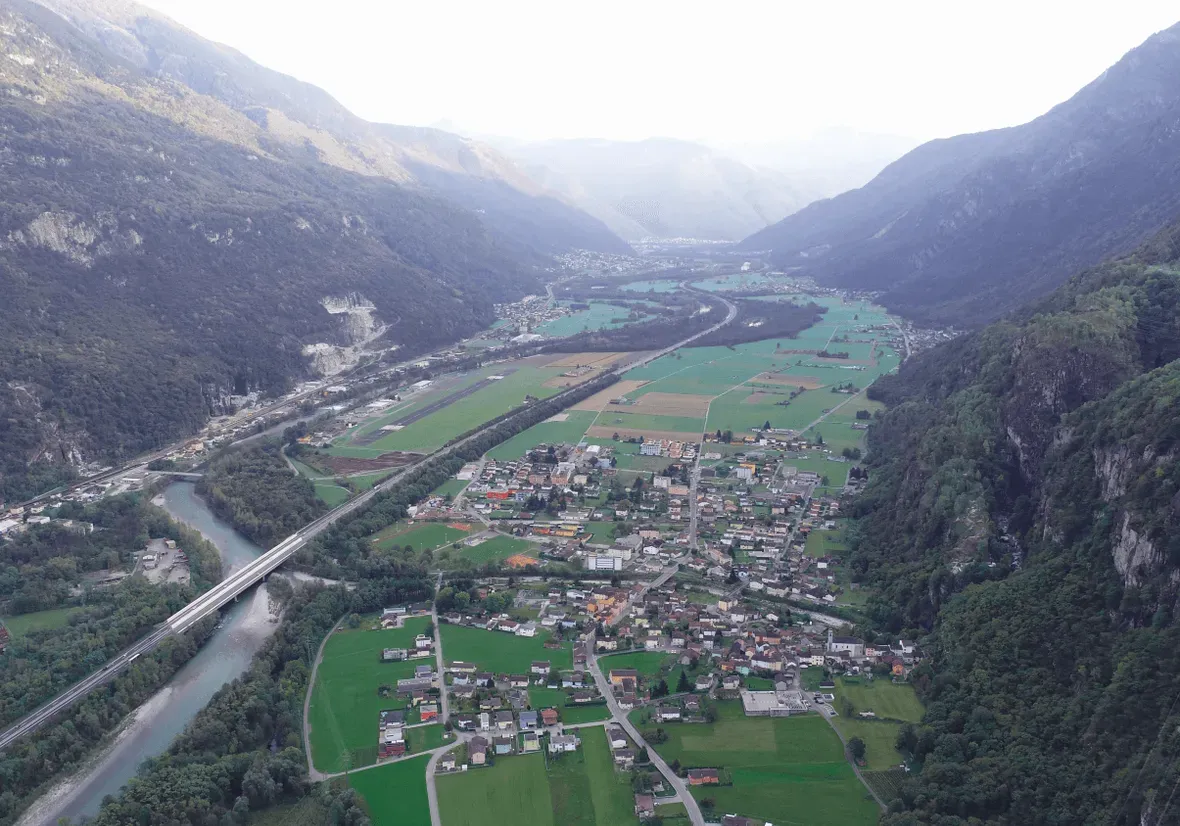 Veduta dall'alto di un paese in fondo a una valle tra le montagne, con campi, il fiume e l'autostrada